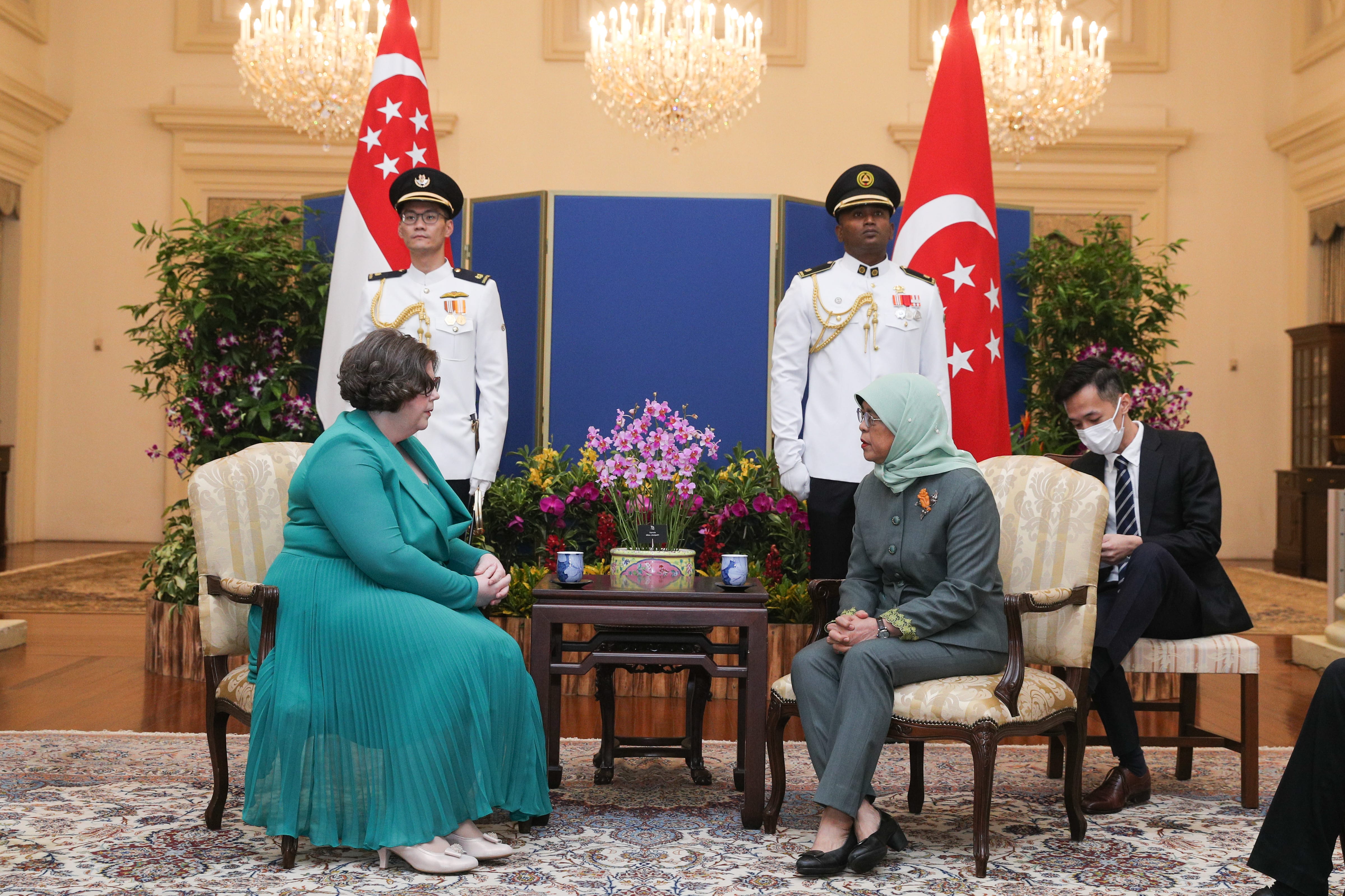Two women sitting in chairs across from each other, Singapore flags in the background.
